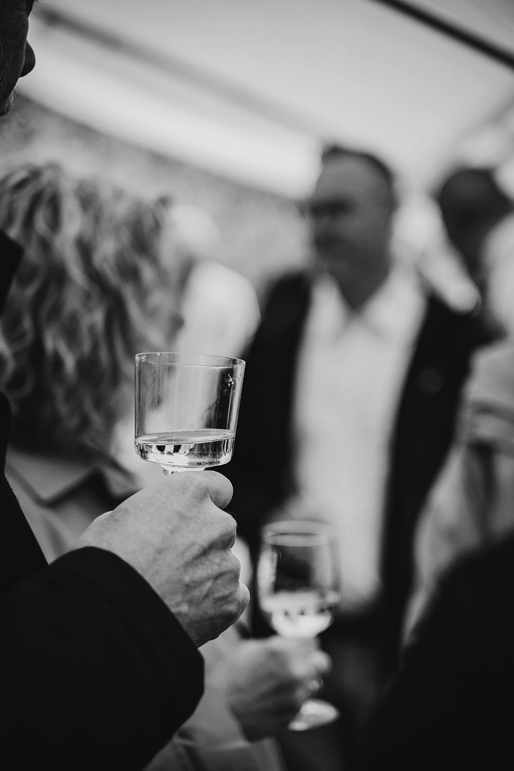 Mingel på bröllopsfest med gäster som skålar i champagneglas. Svartvit bröllopsfoto av bröllopsfotograf Lets Bloom Media i Östergötland.