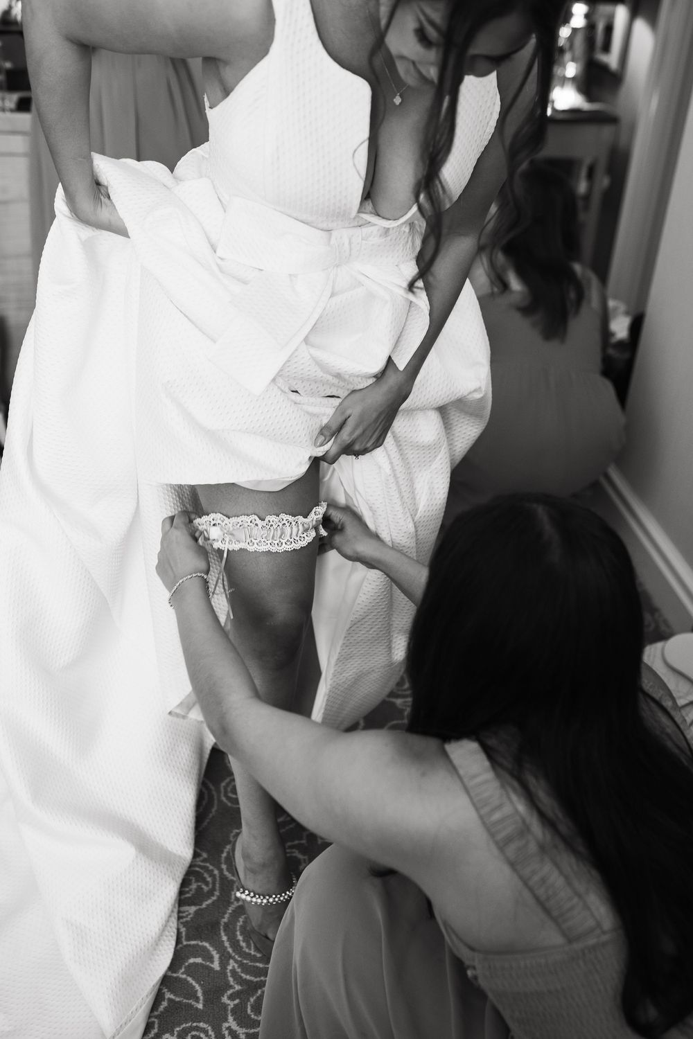 Wedding dress preparation showing garter being adjusted on bride's leg.