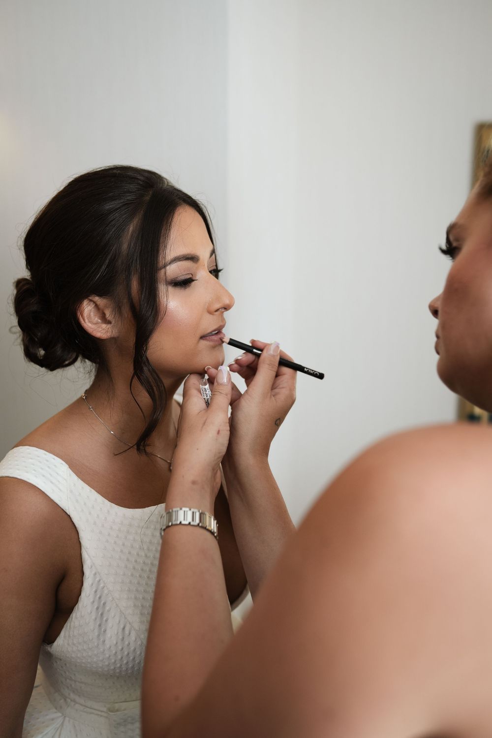 Makeup artist applying lipstick to bride during wedding day preparations.