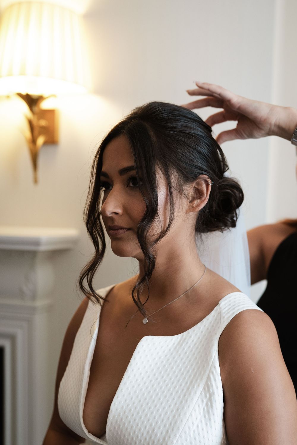 Side profile of bride with elegant updo hairstyle and white textured dress during preparations.