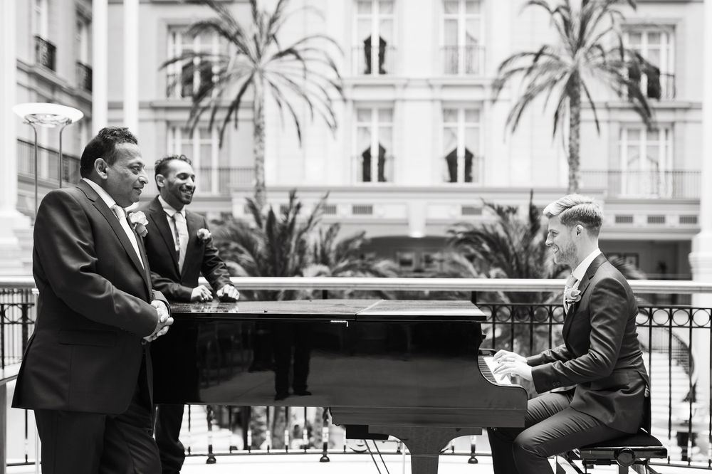 Men gather around grand piano in formal attire at luxurious venue.