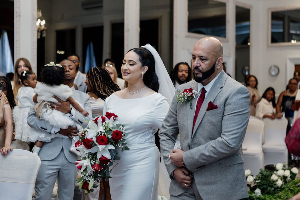Wedding ceremony taking place in a venue with white columns and red rose bouquet at an elegant indoor celebration.