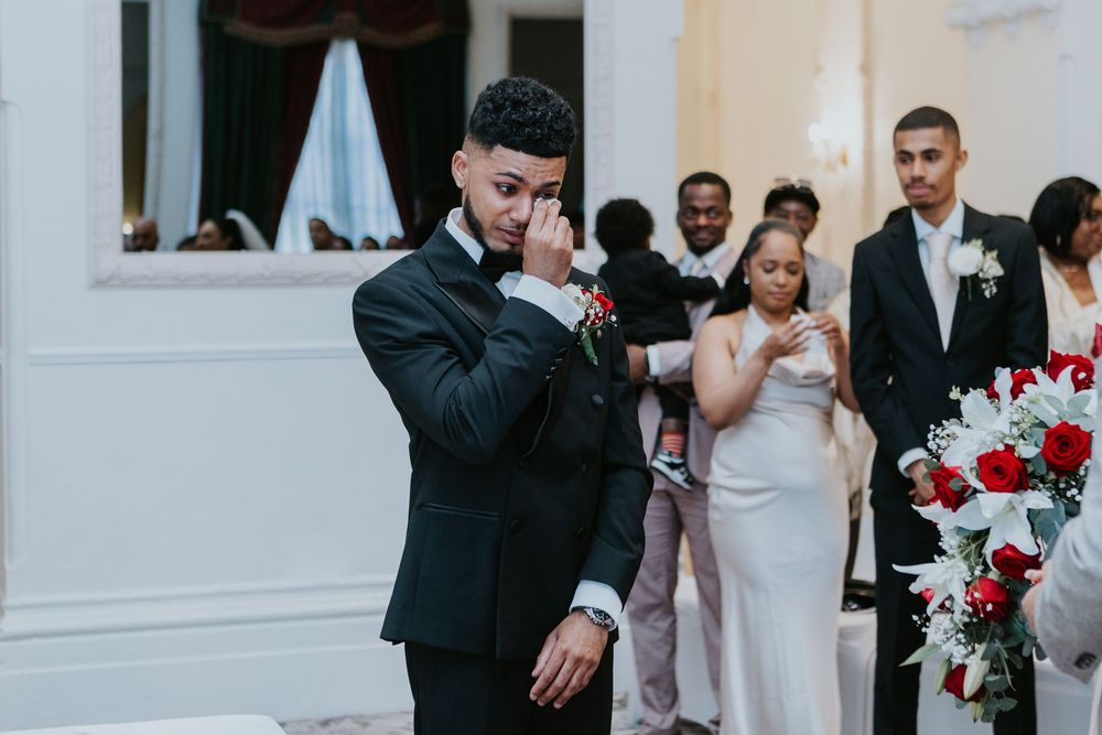 An emotional moment during a wedding ceremony with people gathering near red and white floral decorations.