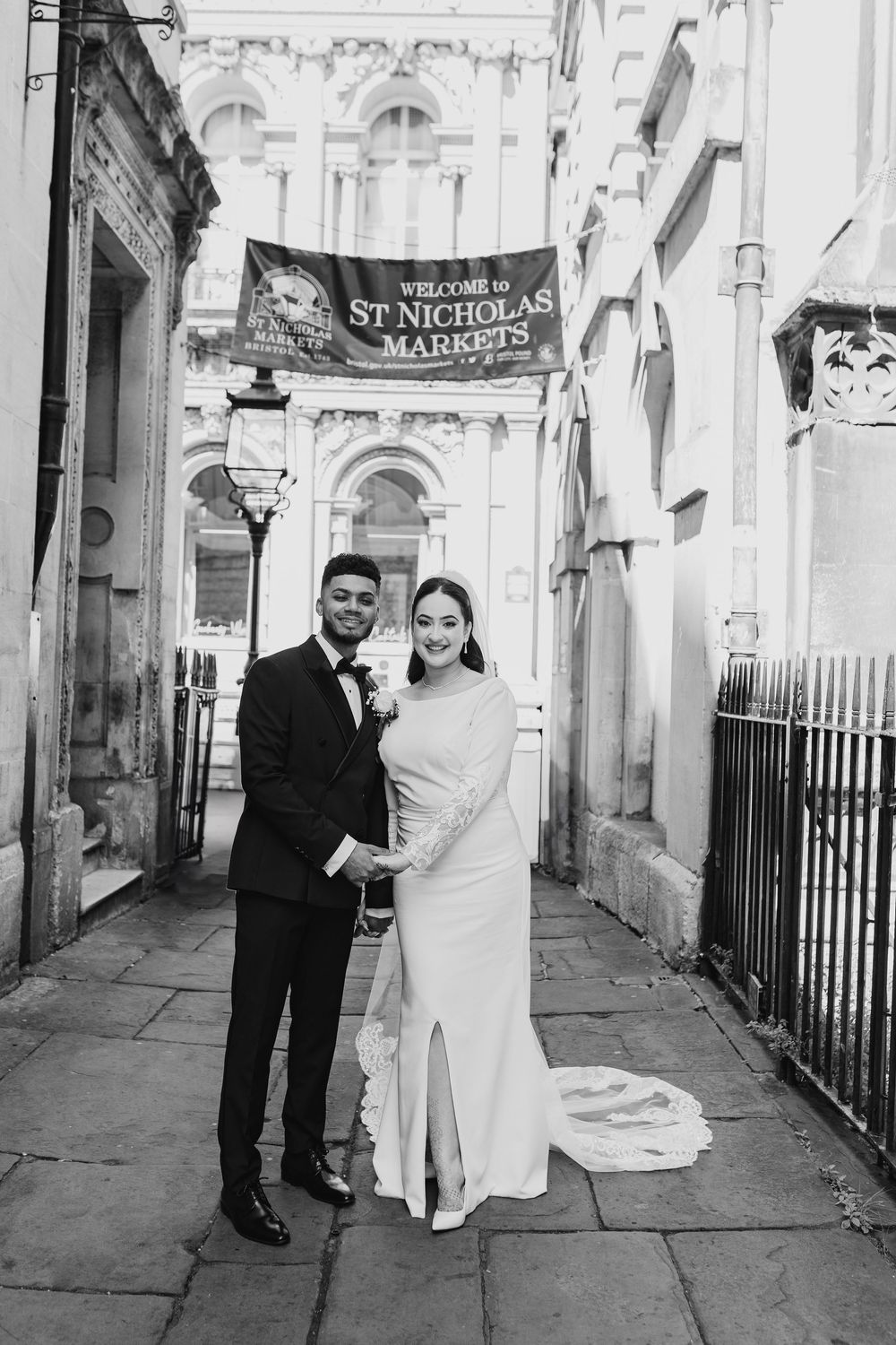 Black and white wedding photo of a couple standing under a St. Nicholas Market sign in historic Bath architecture.