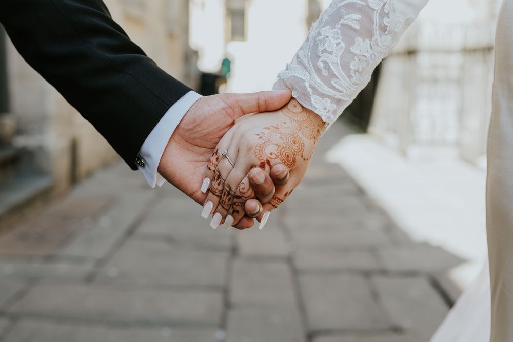 Two hands clasped together in an intimate wedding pose showing lace sleeve and suit jacket details.