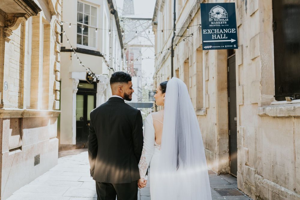 A bride and groom walking down a narrow cobblestone alley between old stone buildings.