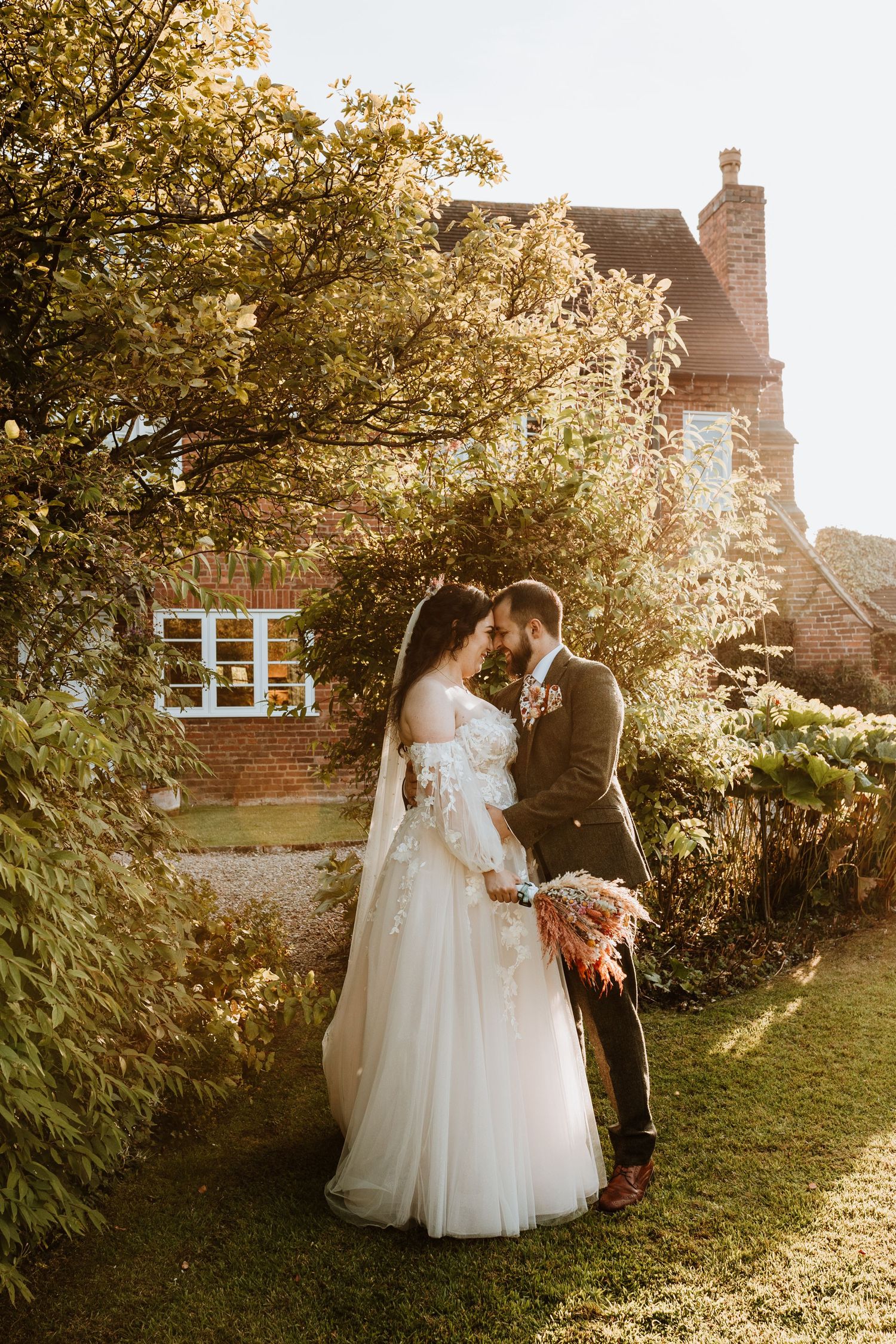 A golden sunset illuminates a couple in a garden setting on their wedding day at a brick cottage.