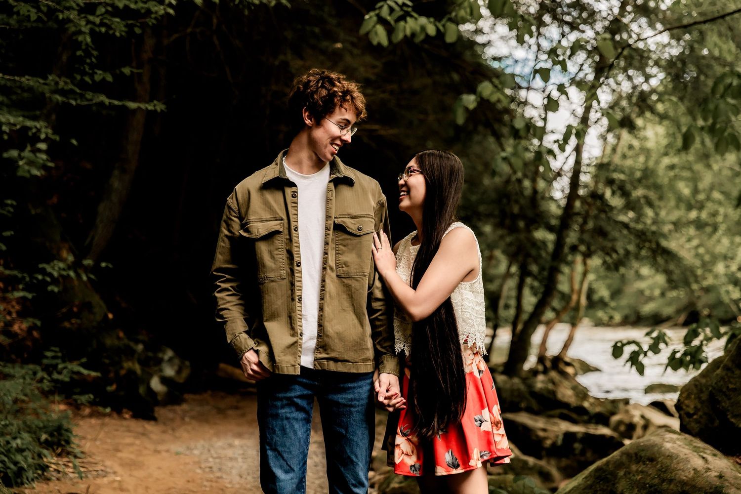 A couple shares a romantic moment while standing on a forest trail next to a rushing stream.