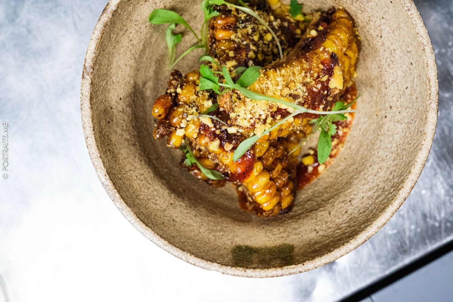 Grilled corn dish garnished with herbs and spices served on rustic ceramic plate.