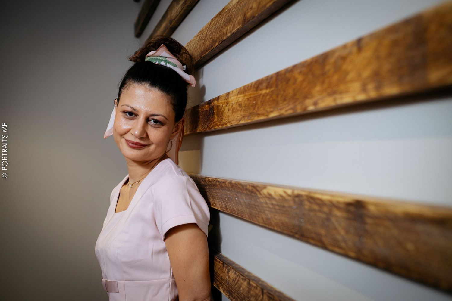 A staff member in uniform standing against a rustic wooden wall background.