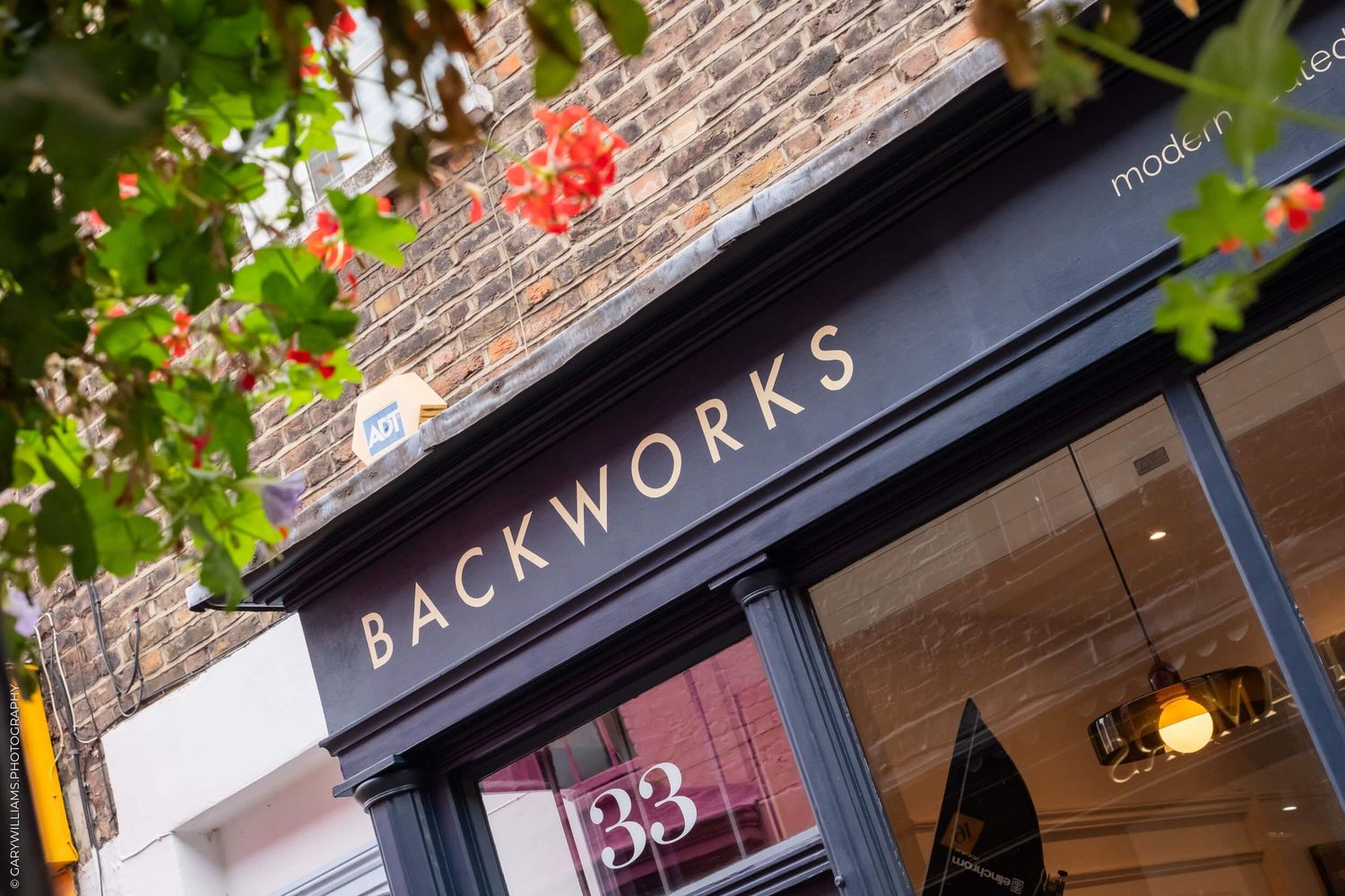 Backworks storefront sign with red flowers and brick facade.