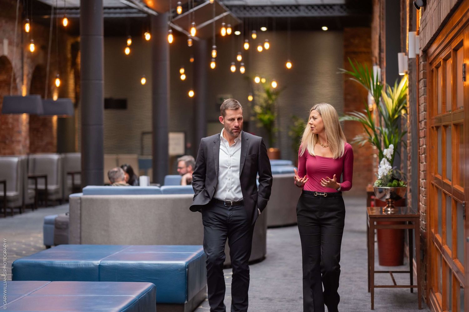 People walking through a modern indoor space with hanging pendant lights.