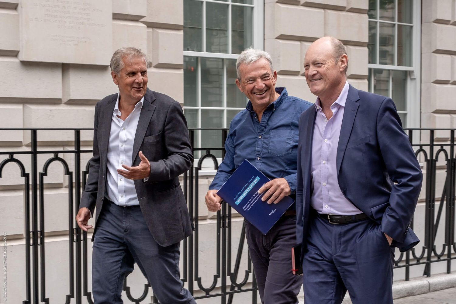 Three business colleagues share laughs while walking outside office building.