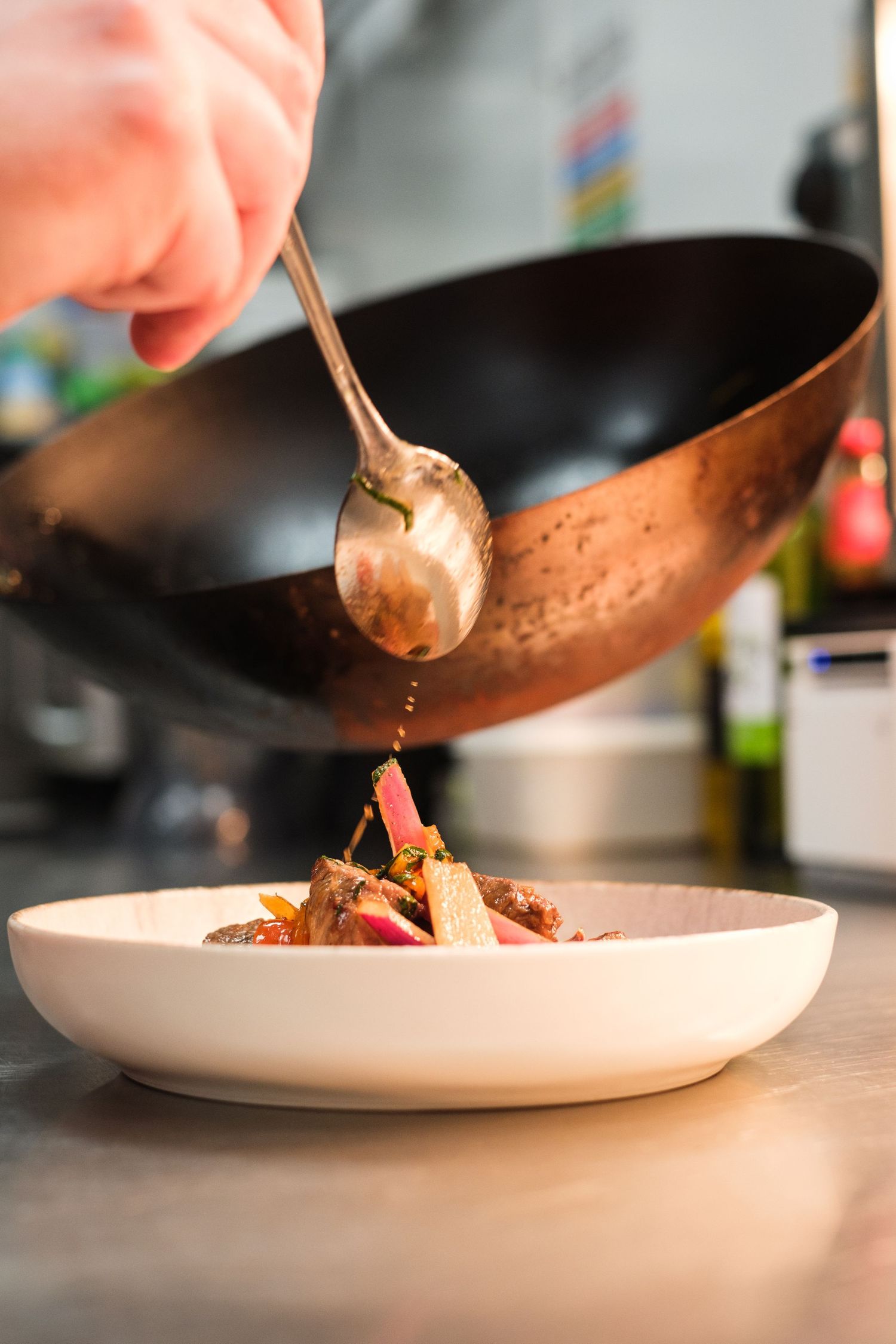 Chef pouring sauce from a copper pan onto a plated dish.