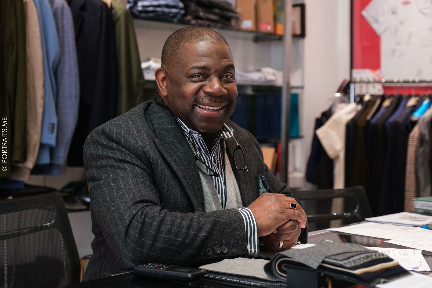 Business owner sits at desk in retail clothing store with welcoming smile.