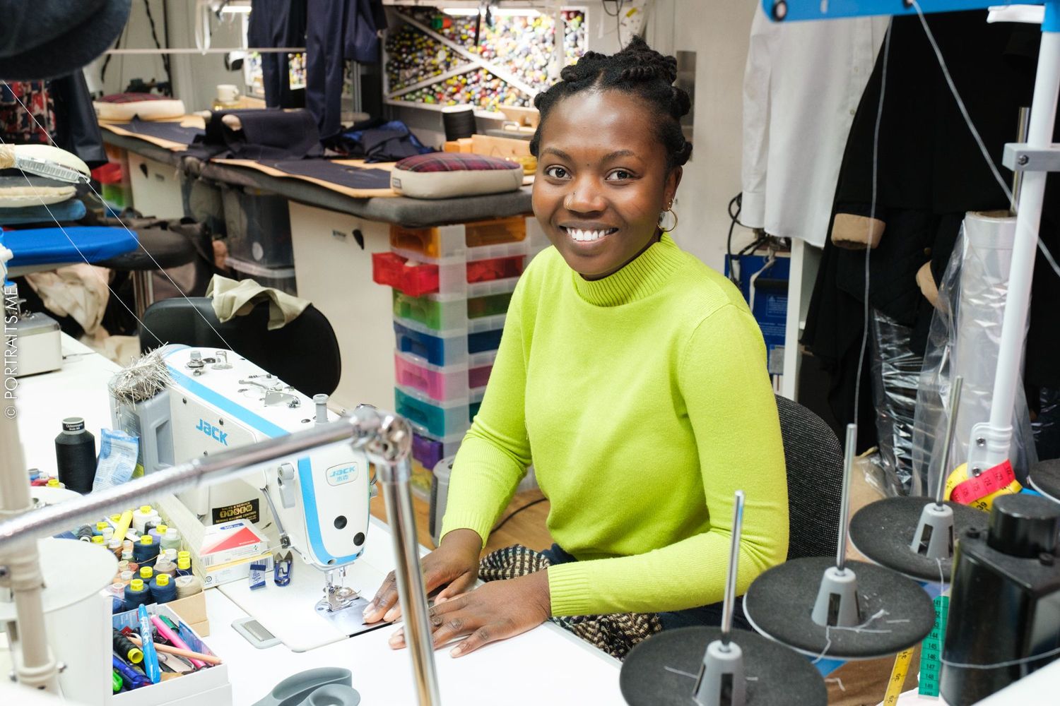 Seamstress in bright yellow sweater working at sewing machine in studio workshop.