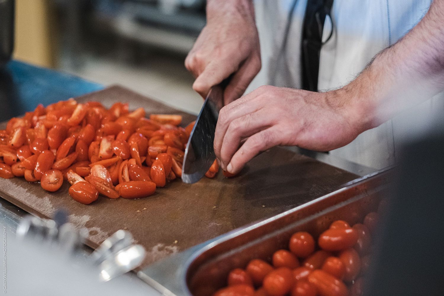 Chef chopping fresh tomatoes on a cutting board in a commercial kitchen.