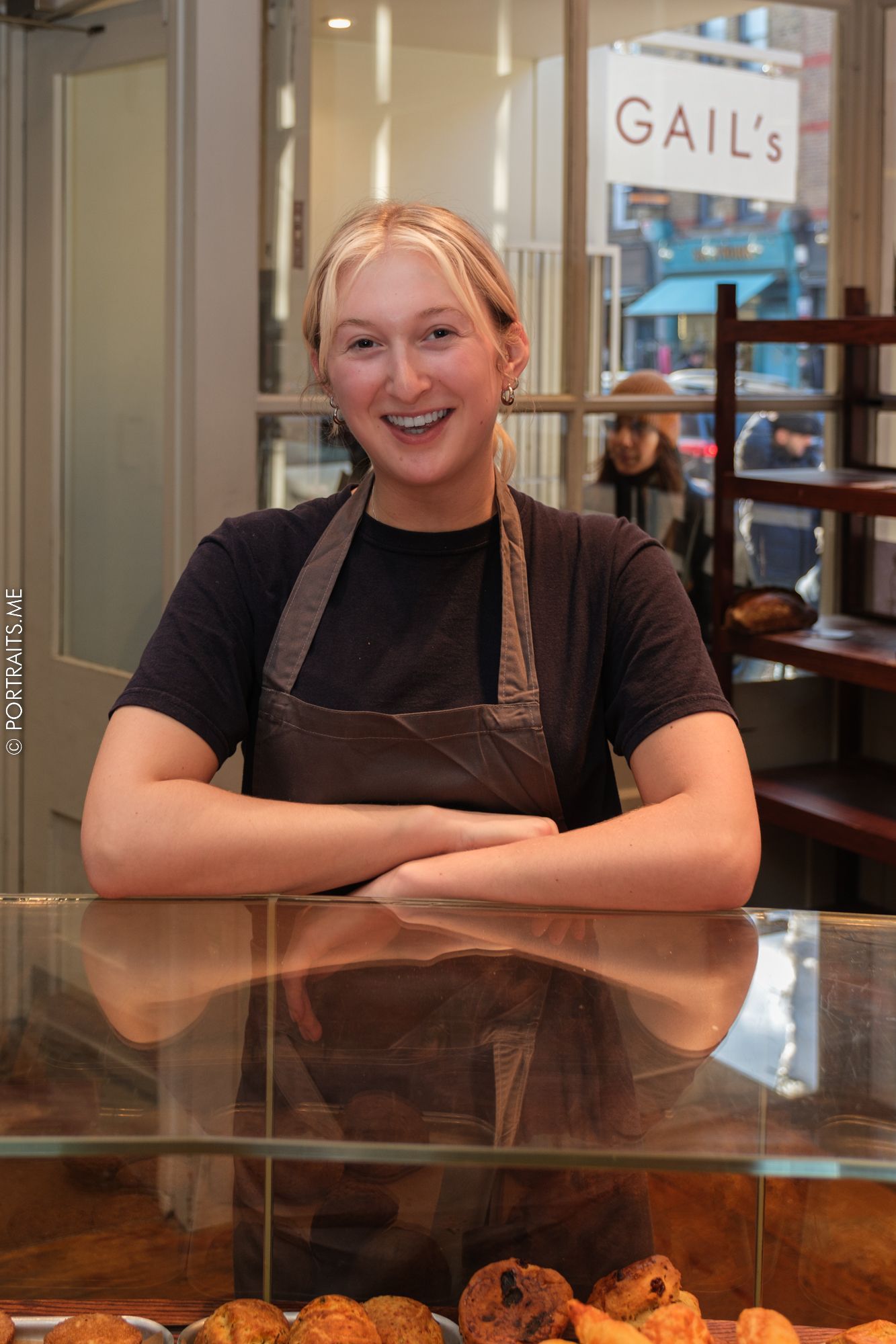 Staff member stands behind counter at Gail's bakery display case.