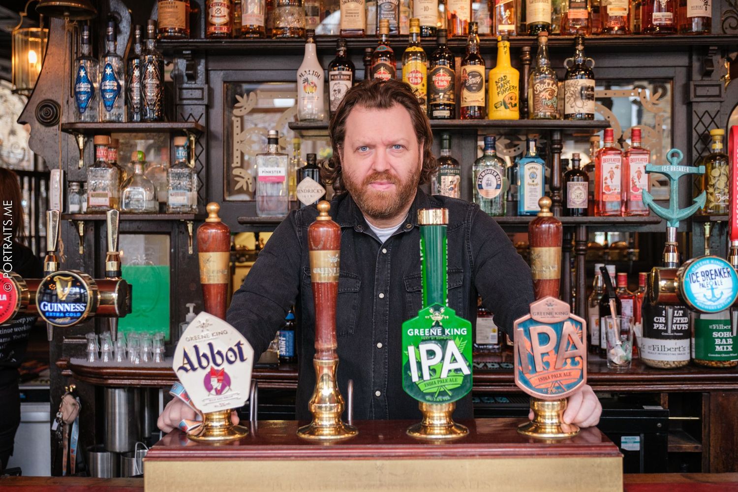 Bartender stands behind bar counter with various beer taps and liquor bottles.