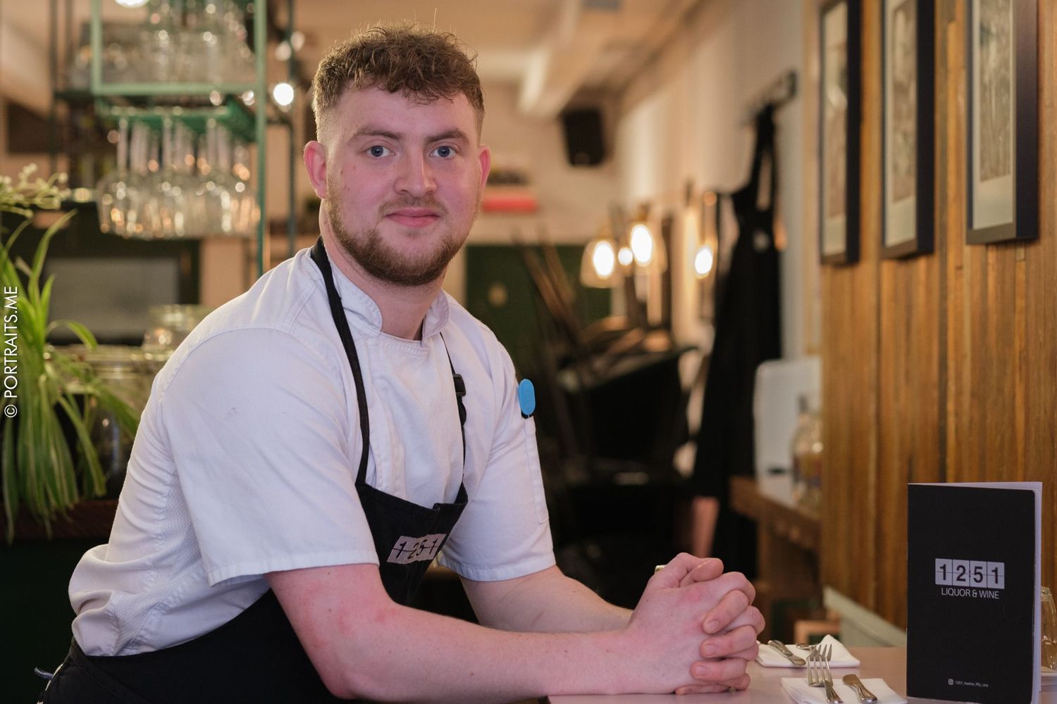 Restaurant worker in white uniform sits at counter in casual dining setting.
