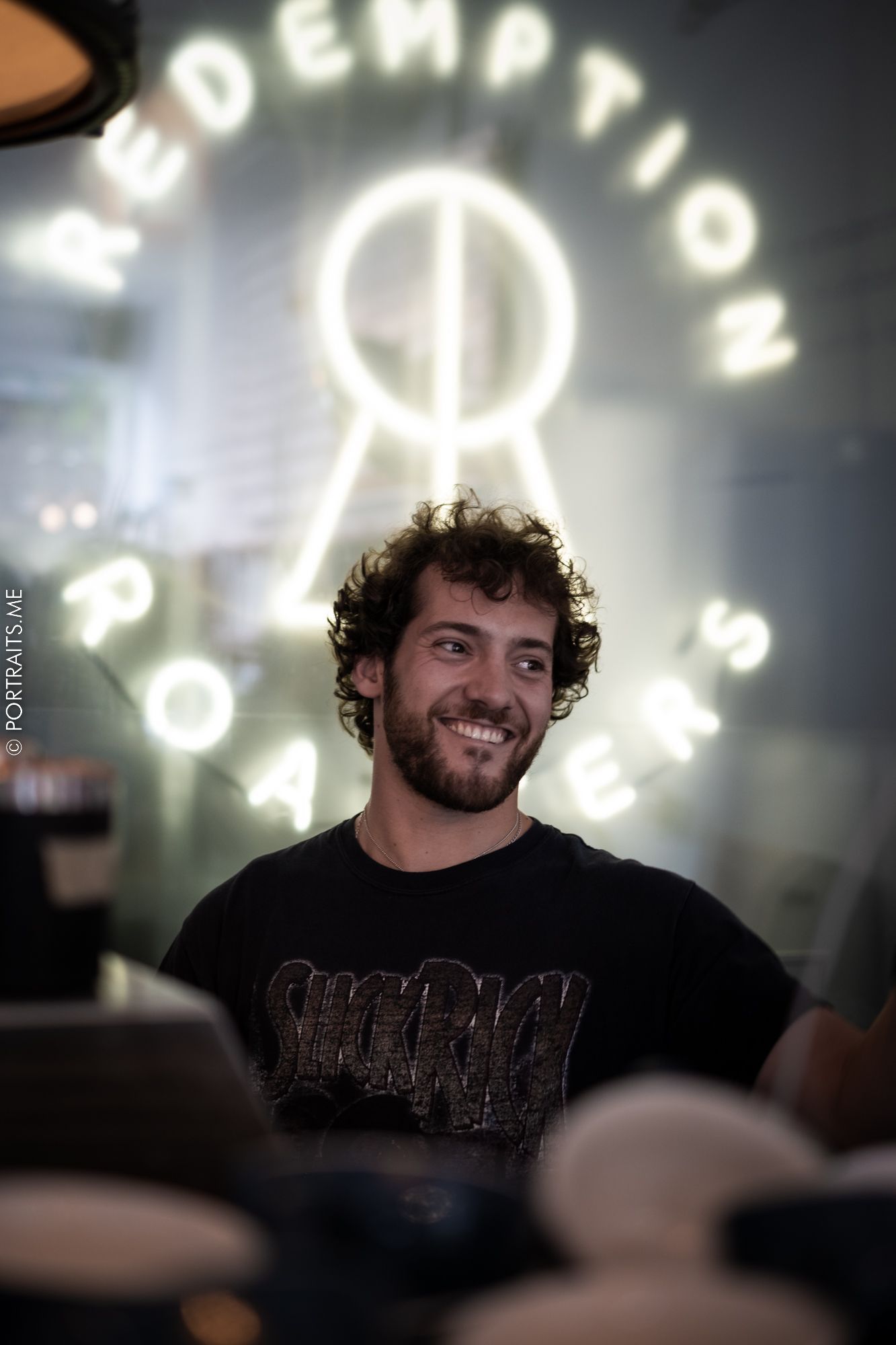 Person smiling in front of illuminated neon redemption sign at arcade or entertainment venue.