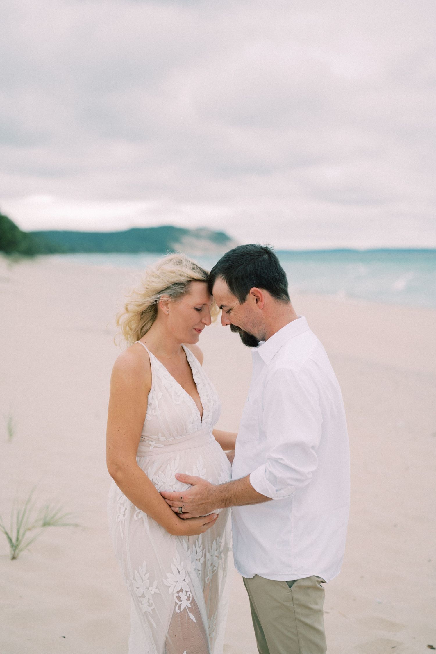 Intimate maternity beach photo of couple embracing on sandy shore.