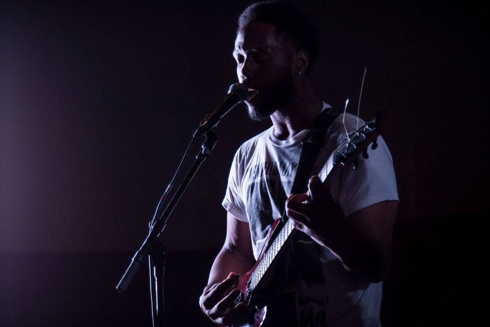 Silhouette of musician performing with guitar and microphone in dark lighting.
