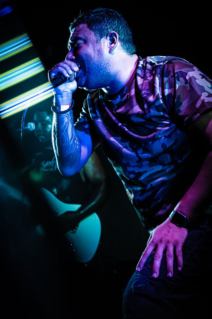 Concert performer in camouflage shirt singing into microphone under dramatic blue stage lighting.