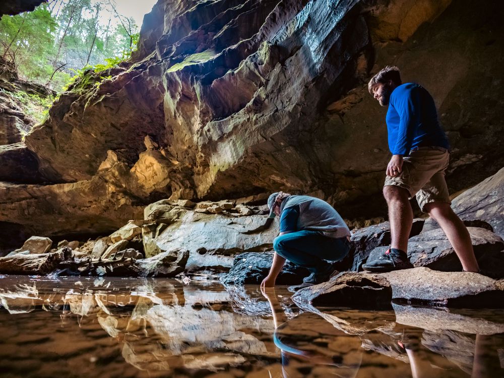 Adventurers exploring wet cave floor with dramatic rock formations overhead.