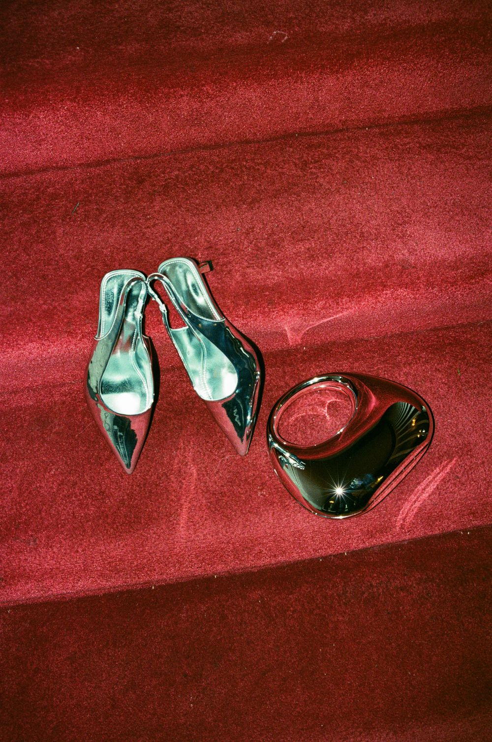 A pair of black patent leather high heel shoes and a handbag displayed on red carpet.
