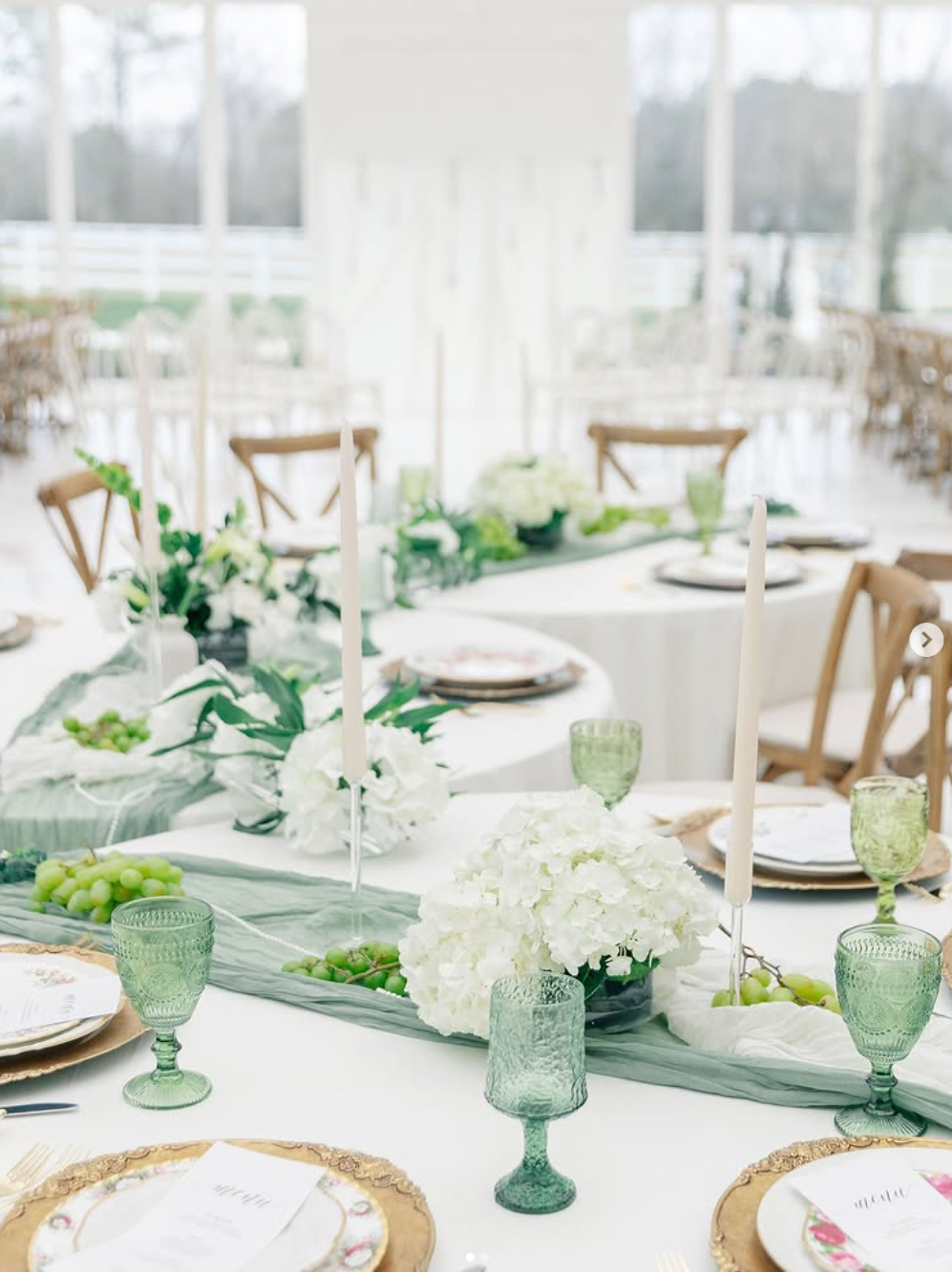 Elegant wedding table setting with sage green runners, white hydrangeas, and vintage-inspired green glassware.
