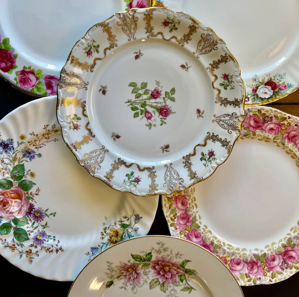 Four vintage floral china plates with gold trim and pink rose patterns displayed together on a white surface.