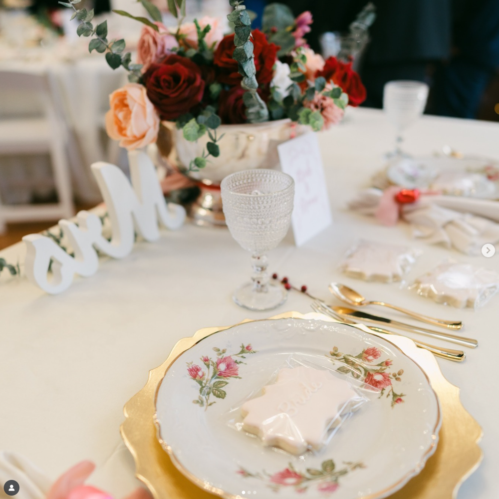 Elegant table setting with floral china plate, gold charger, crystal glassware and coral flower centerpiece arrangement.