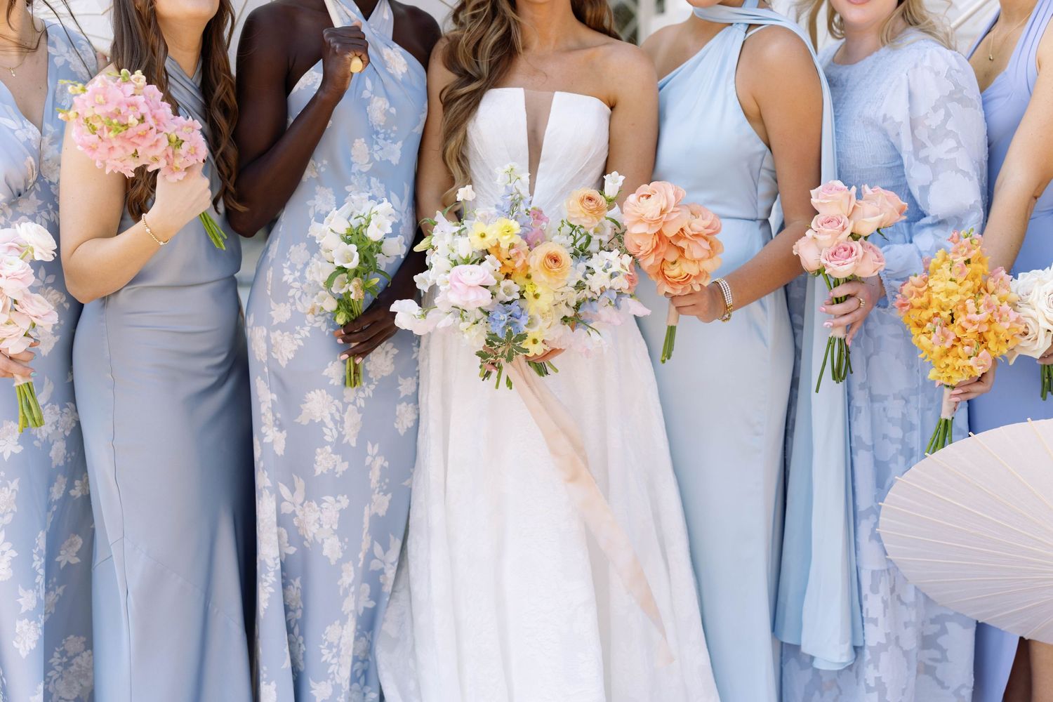 Bridesmaids wearing light blue dresses hold colorful bouquets of peach, pink and white flowers at a wedding.