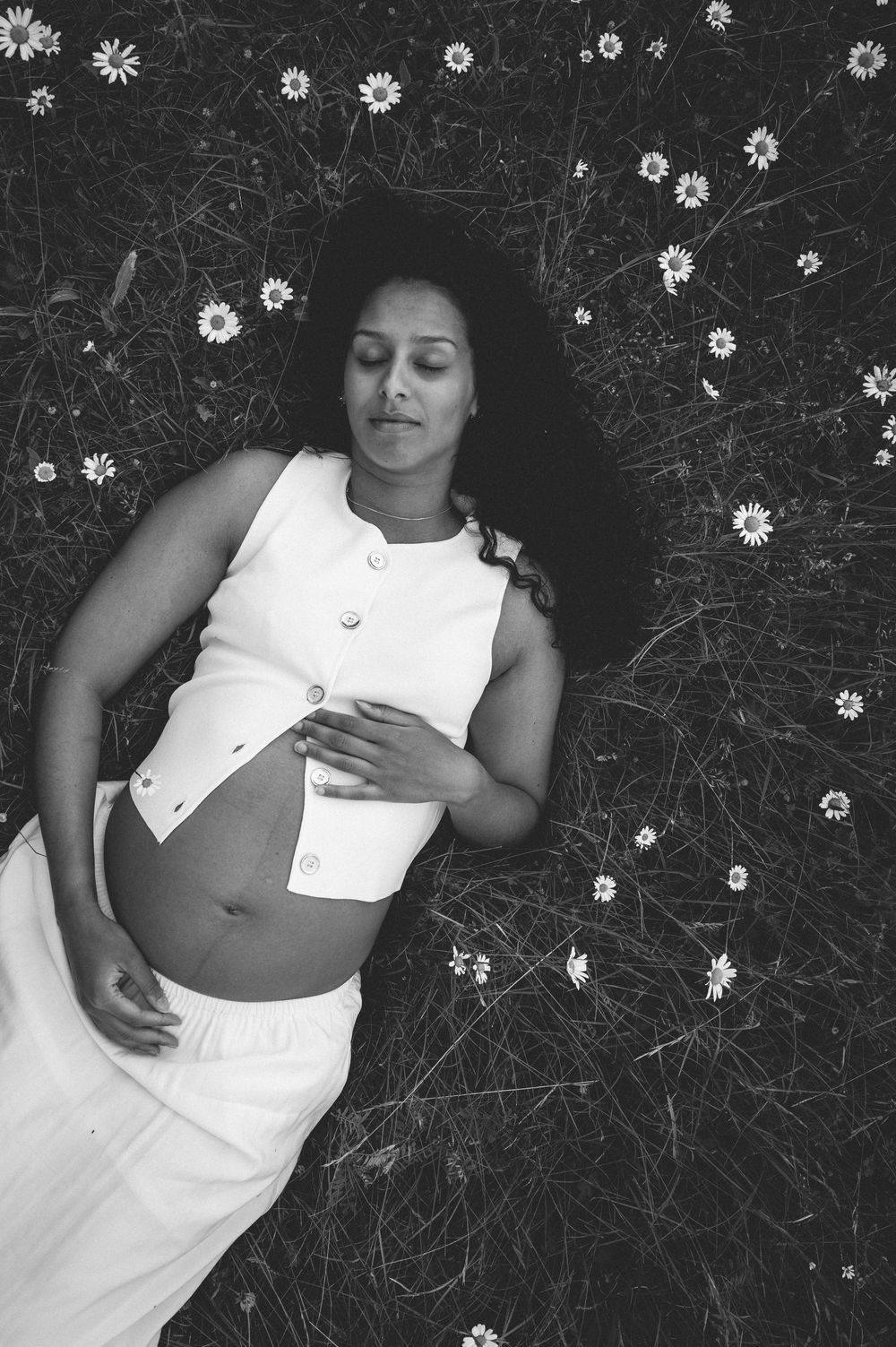 A woman in a white dress lies peacefully among delicate daisies in a black and white artistic composition.
