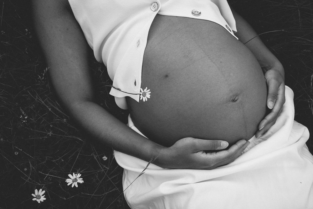 A series of black and white maternity photos showing a pregnant woman's belly with white fabric draping.