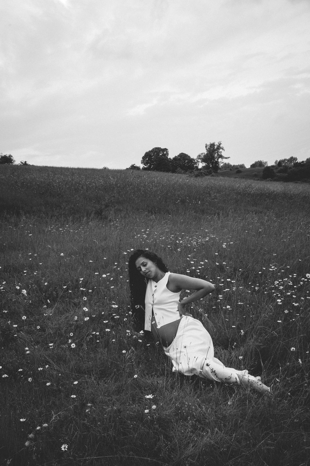 Black and white landscape shows a figure in white resting among daisies in a rolling meadow.
