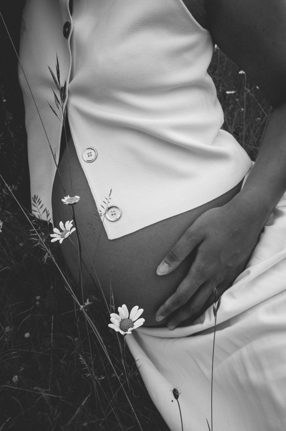 A series of black and white photographs showing someone in white clothing sitting among delicate wildflowers and grass.