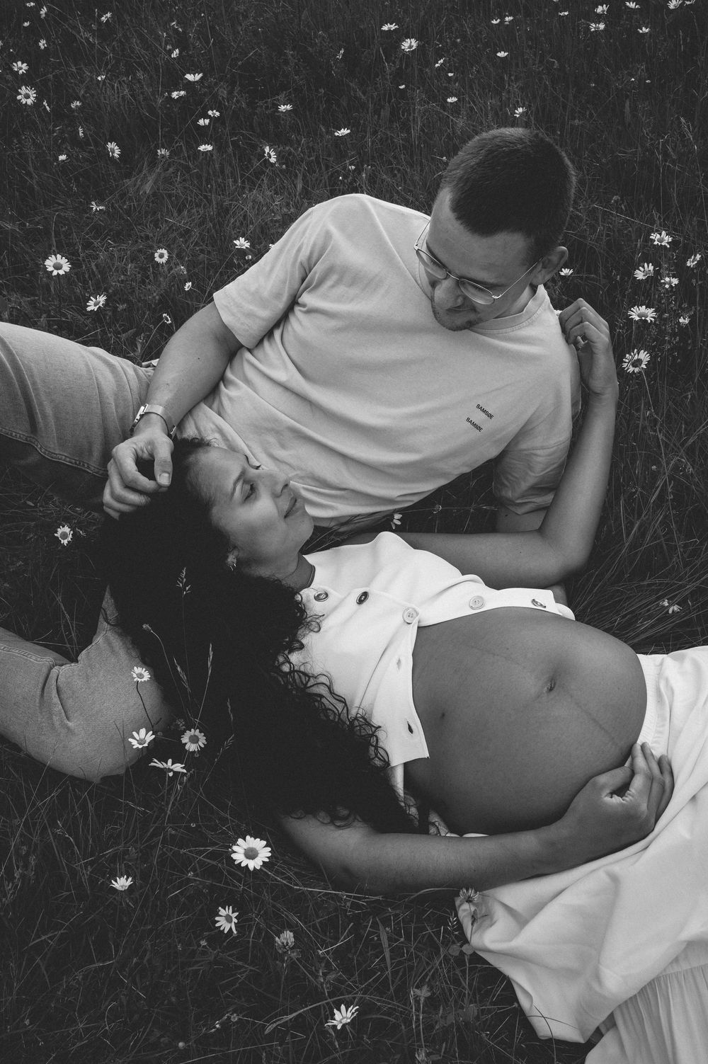 Black and white photograph of two people lying in grass with small white flowers.