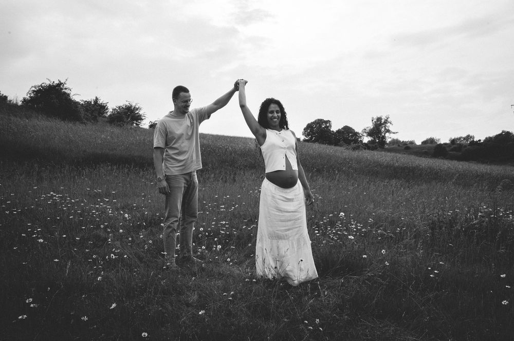 Black and white photograph of a couple holding hands and celebrating in a wildflower meadow at sunset.