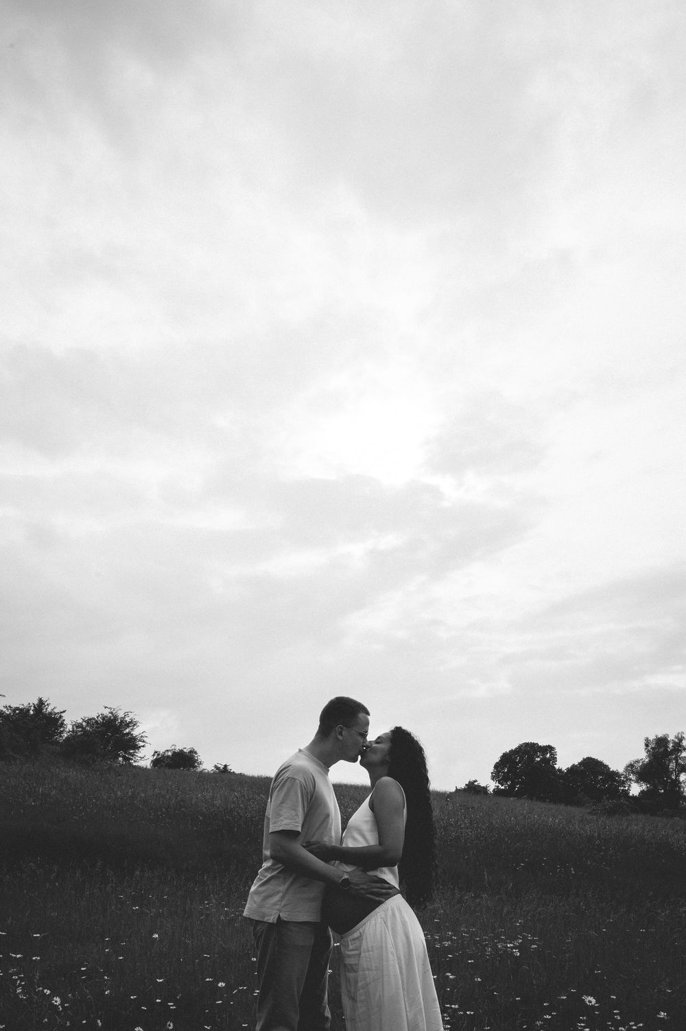 A black and white photo series shows a couple sharing romantic moments in a meadow under cloudy skies.