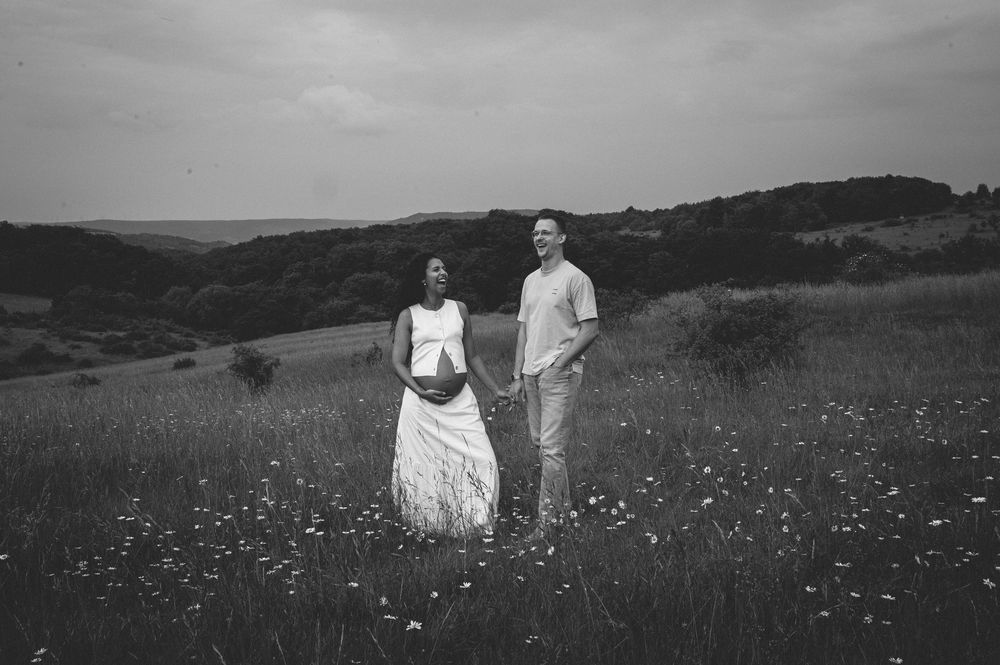 A couple stands in a wildflower meadow against rolling hills in dramatic black and white photography.