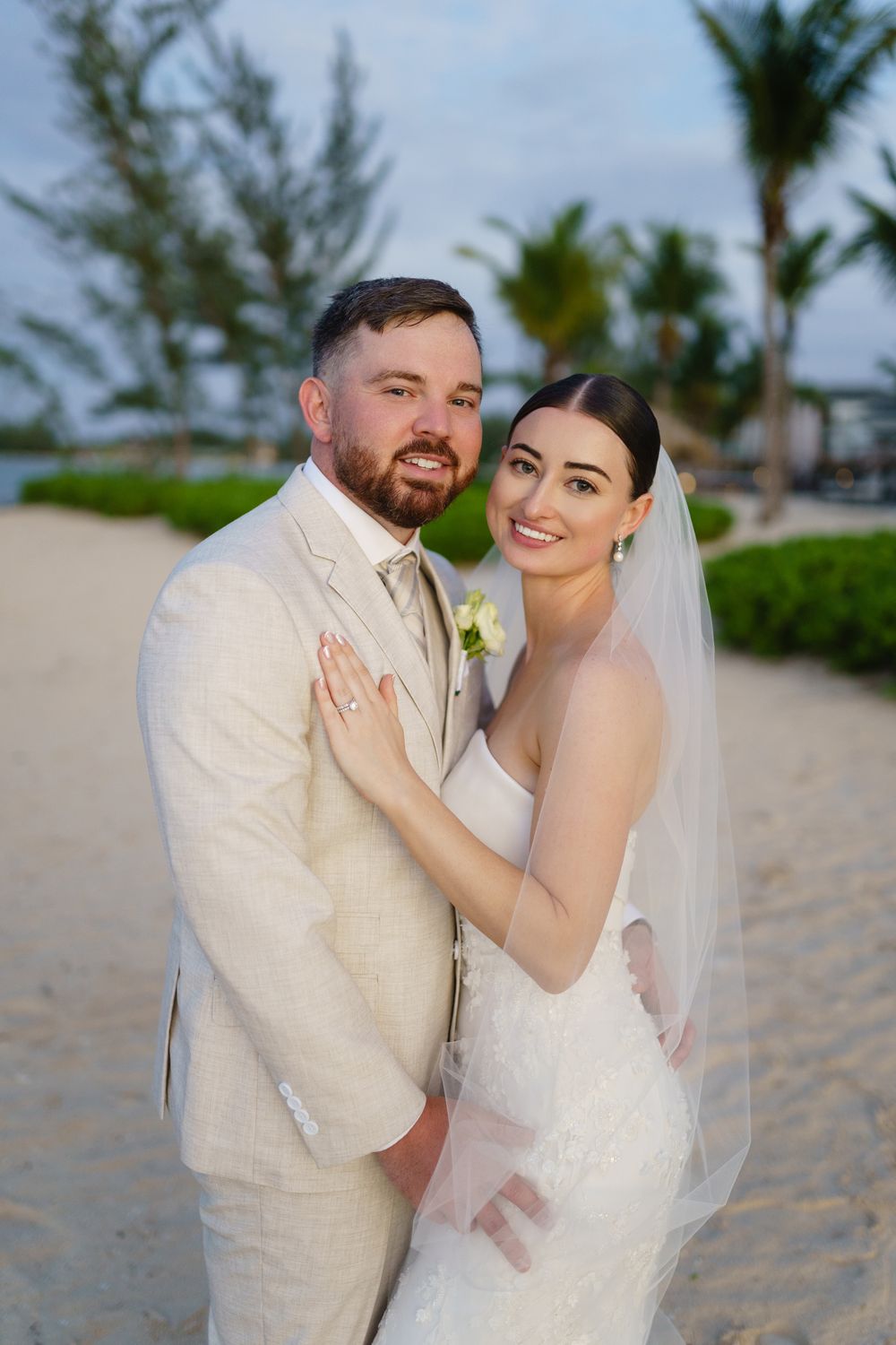 A couple poses together on a tropical beach during their destination wedding with palm trees in the background.