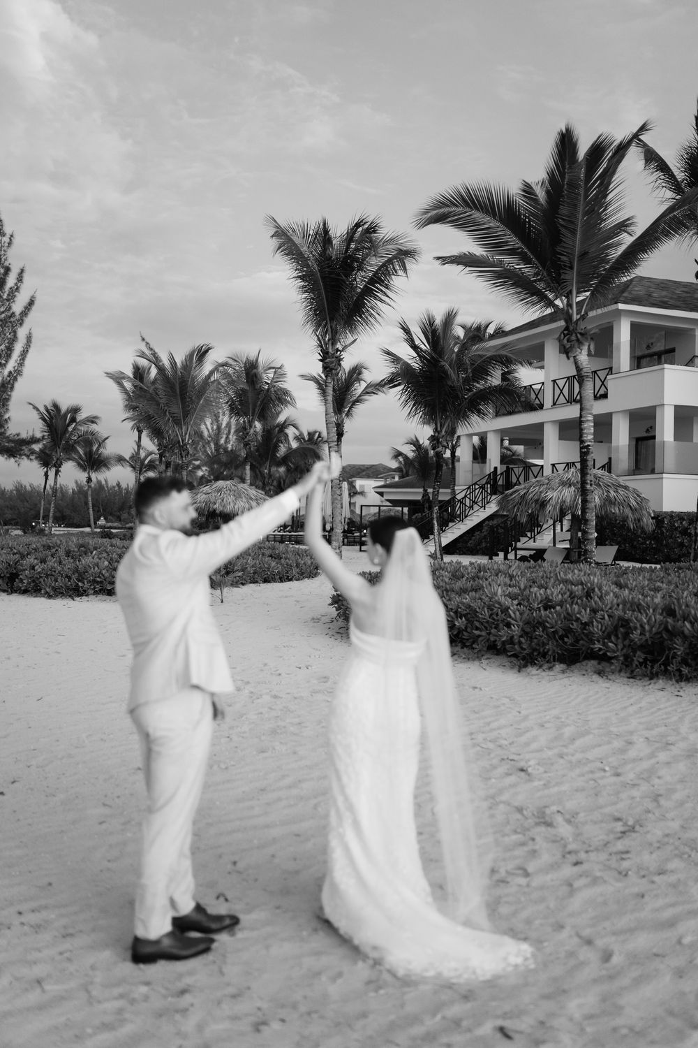 A series of black and white photos showing a couple in white attire walking along a tropical beach with palm trees.