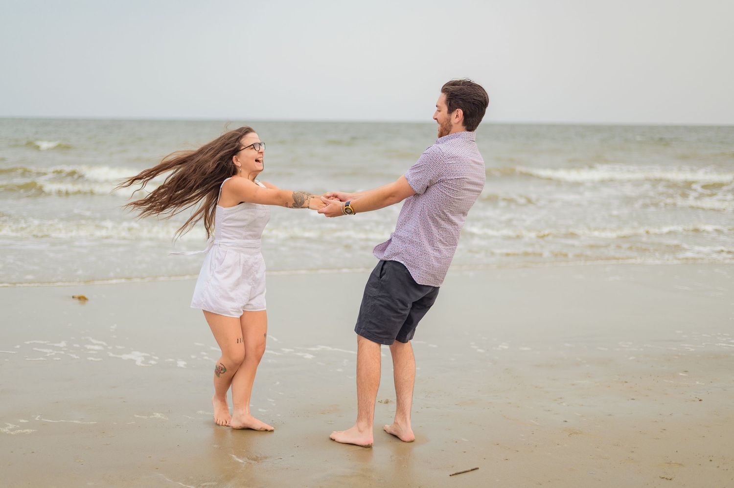 Couple dancing barefoot on the beach with waves in the background.