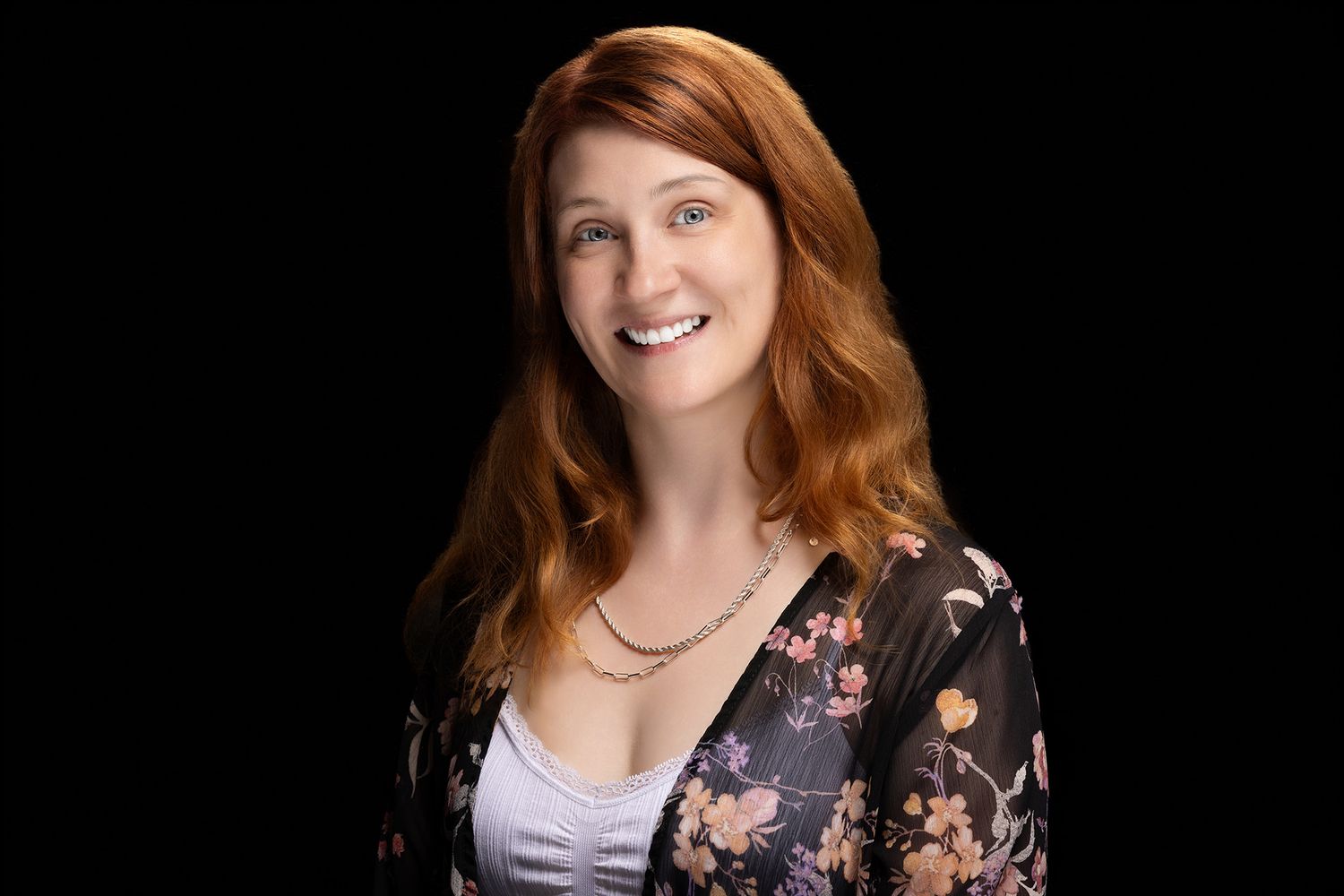 A person with curly hair wearing a black shirt smiles at the camera in a professional headshot style photo.
