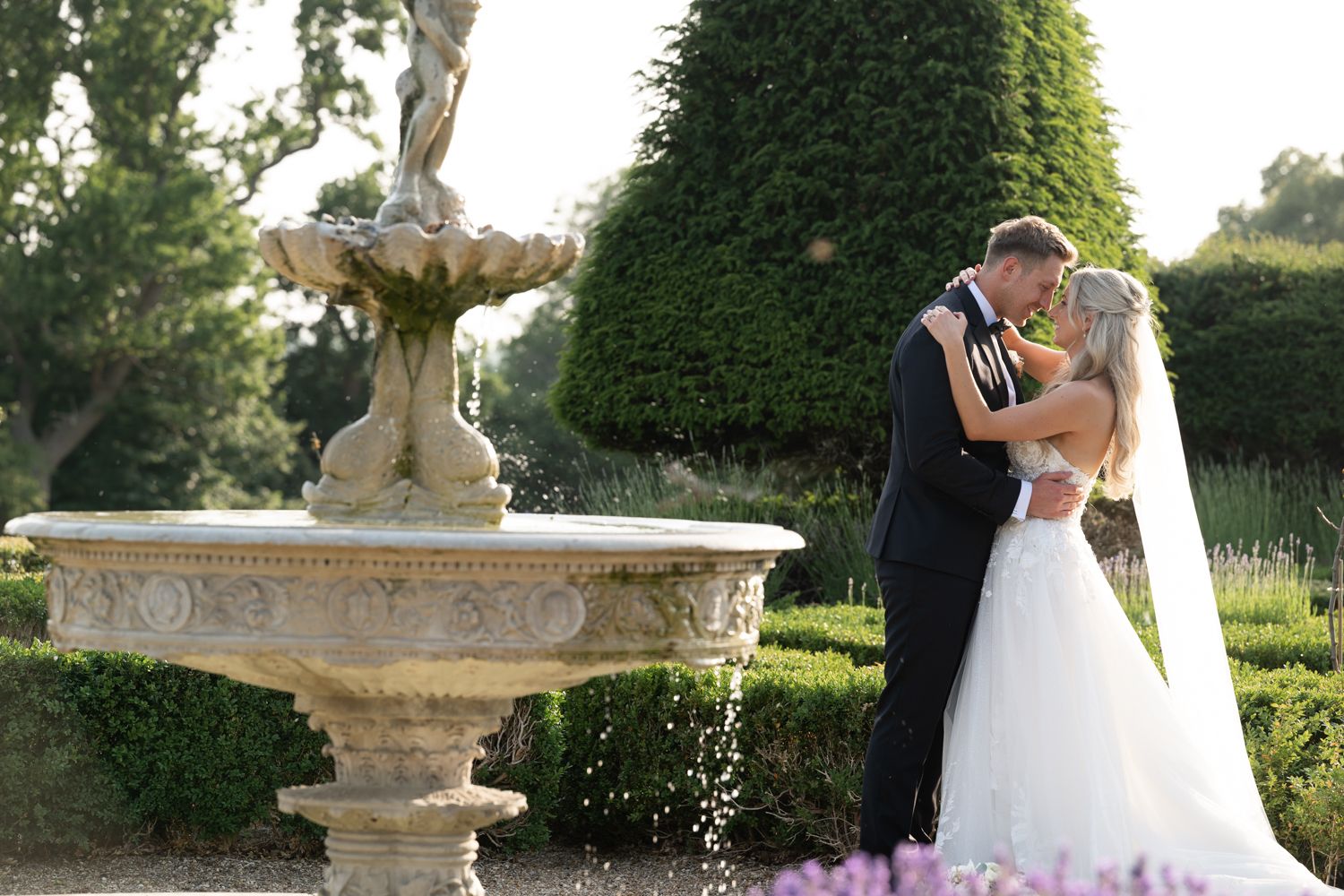 A romantic garden ceremony featuring silhouettes of a couple kissing beneath an ornate arch and fountain.