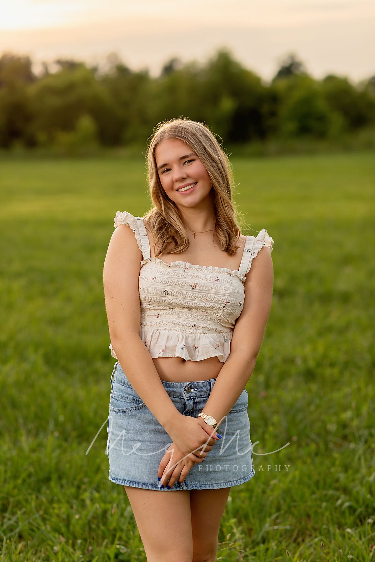 Teen in ruffled crop top and denim skirt poses outdoors in a grassy field during golden hour. Senior Pictures with MegMc Photography, Medina