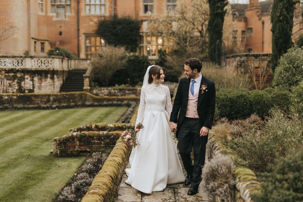 Couple shares romantic moment in elegant garden setting surrounded by stone architecture and manicured grounds.