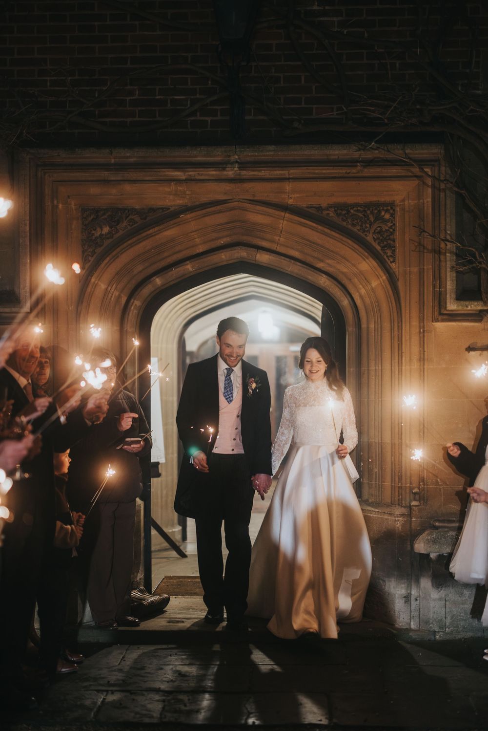 A newlywed couple exits through a gothic archway as guests hold sparklers creating a magical ambiance.